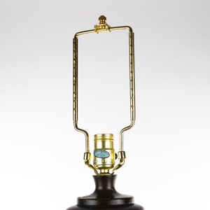 May include: A gold metal lamp base with a round, dark brown shade. The lamp base has a decorative design and a standard light bulb socket.