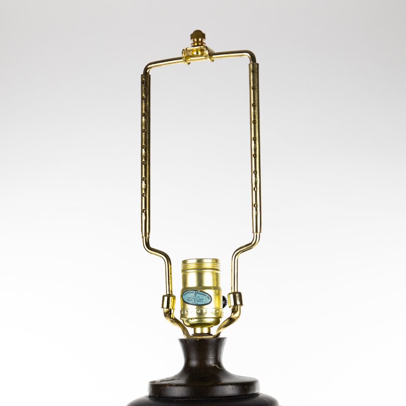 May include: A gold metal lamp base with a round, dark brown shade. The lamp base has a decorative design and a standard light bulb socket.