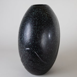 May include: A black ceramic vase with a speckled green glaze. The vase has a rounded, egg-like shape with a smooth, glossy finish.
