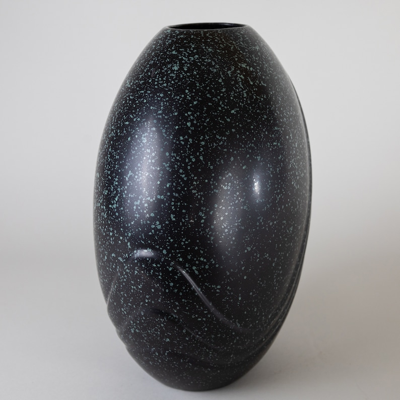 May include: A black ceramic vase with a speckled green glaze. The vase has a rounded, egg-like shape with a smooth, glossy finish.
