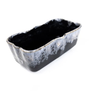 May include: Black ceramic planter with a white and gold glaze. The planter has a rectangular shape with a wavy edge.