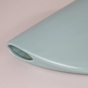 May include: A light blue ceramic vase with a unique, curved design. The vase has a wide opening and a narrow base.