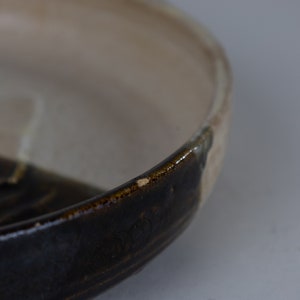 May include: A ceramic bowl with a dark brown glaze on the bottom half and a light beige glaze on the top half.