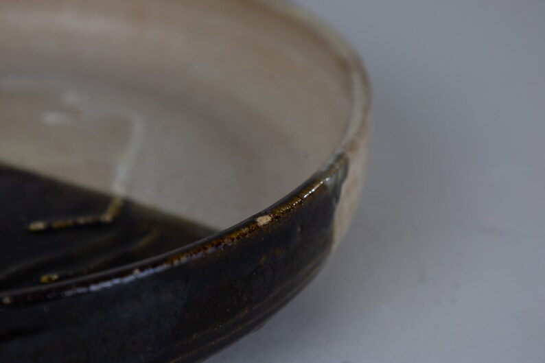May include: A ceramic bowl with a dark brown glaze on the bottom half and a light beige glaze on the top half.