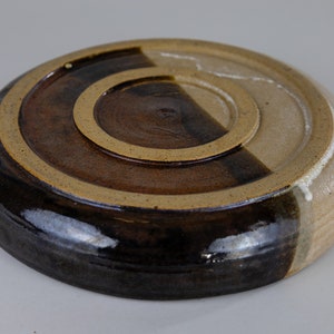 May include: The underside of a ceramic plate, glazed in brown and tan. The plate is divided in half, with one side a darker brown and the other a lighter tan.
