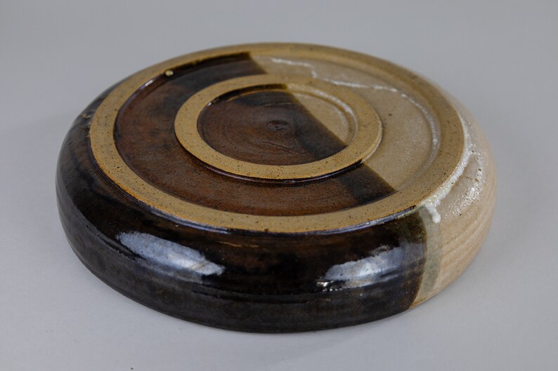 May include: The underside of a ceramic plate, glazed in brown and tan. The plate is divided in half, with one side a darker brown and the other a lighter tan.