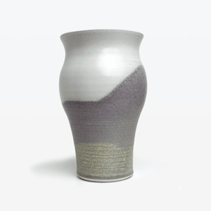 May include: A white ceramic vase with a gray and beige glaze. The vase has a rounded body and a flared lip.