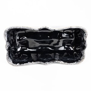 May include: A black ceramic serving dish with a wavy, scalloped edge. The dish is glazed and has a shiny finish.