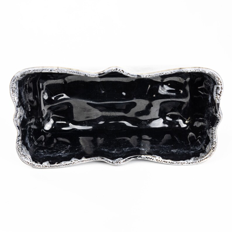 May include: A black ceramic serving dish with a wavy, scalloped edge. The dish is glazed and has a shiny finish.