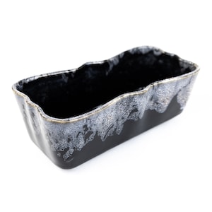 May include: Black ceramic planter with a white and gold speckled glaze. The planter has a rectangular shape with a wavy rim.