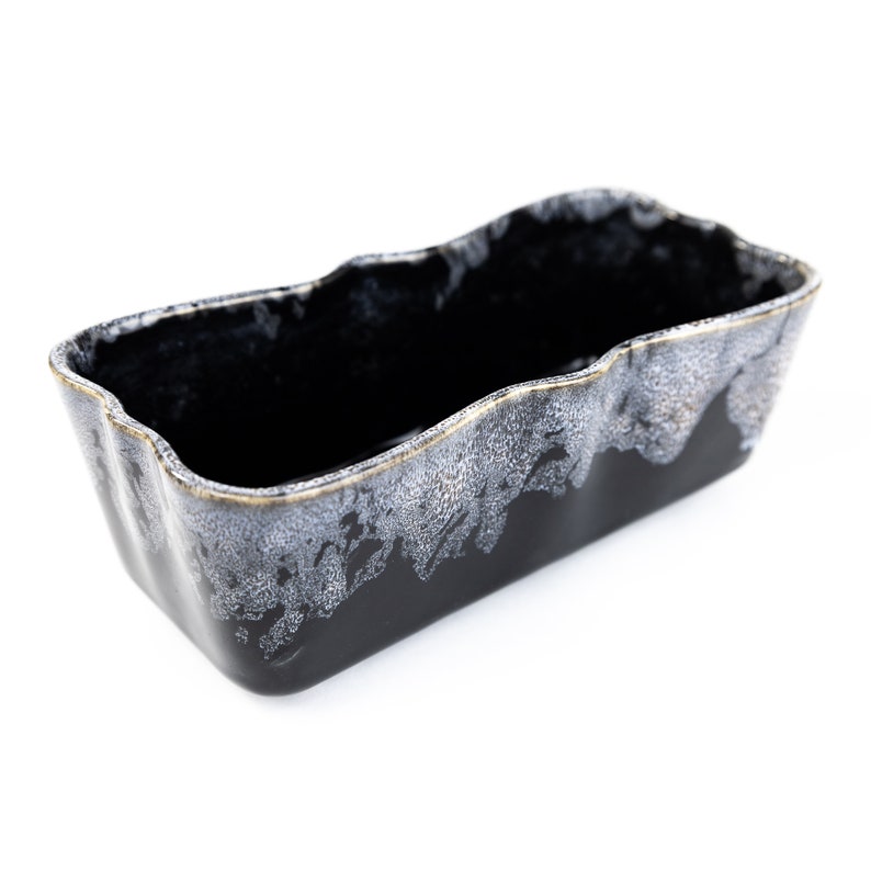 May include: Black ceramic planter with a white and gold speckled glaze. The planter has a rectangular shape with a wavy rim.