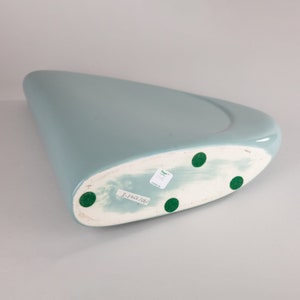 May include: A light blue ceramic vase with a unique, curved shape. The vase has a sticker on the bottom with the text "Hager" and "8-244/1081".
