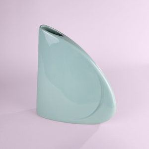May include: A light blue ceramic vase with a unique, curved shape. The vase has a smooth, glossy finish.