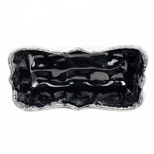 May include: A black ceramic rectangular serving dish with a wavy, silver-colored rim. The dish is empty and has a glossy finish.