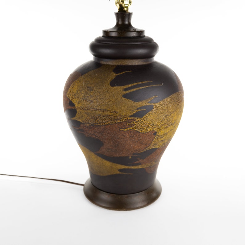 May include: A brown ceramic table lamp with a gold and brown abstract design. The lamp has a round base and a cylindrical shade.