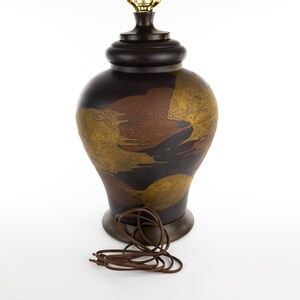 May include: A brown ceramic table lamp with a gold and brown abstract design. The lamp has a brown cord.