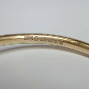 Pu&ograve; includere: Primo piano di un braccialetto dorato. Il braccialetto presenta diversi piccoli marchi stampati. La superficie &egrave; liscia e riflettente. Lo sfondo &egrave; di colore chiaro.