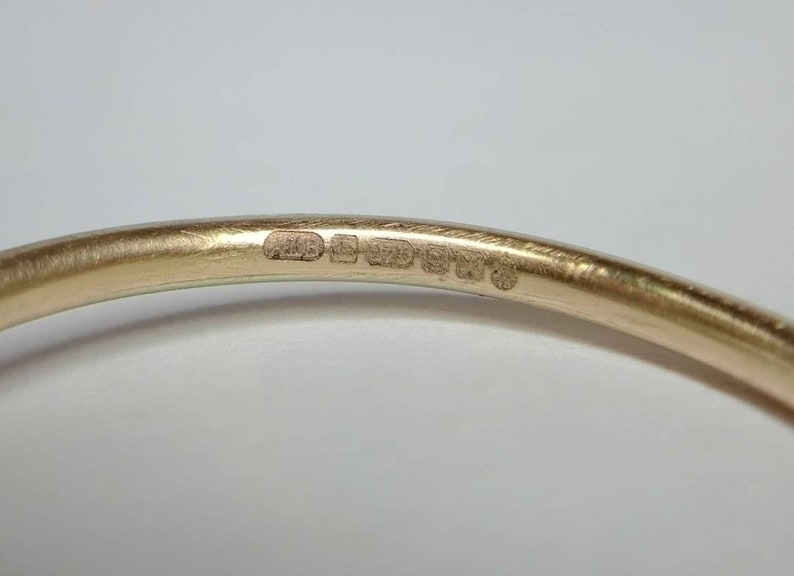 Pu&ograve; includere: Primo piano di un braccialetto dorato. Il braccialetto presenta diversi piccoli marchi stampati. La superficie &egrave; liscia e riflettente. Lo sfondo &egrave; di colore chiaro.