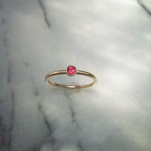 Pu&ograve; includere: Un delicato anello d'oro con una piccola gemma rotonda di colore rosa brillante. L'anello ha una fascia sottile e un design semplice ed elegante. La gemma &egrave; incastonata in una lunetta, aggiungendo un tocco di colore allo stile minimalista.