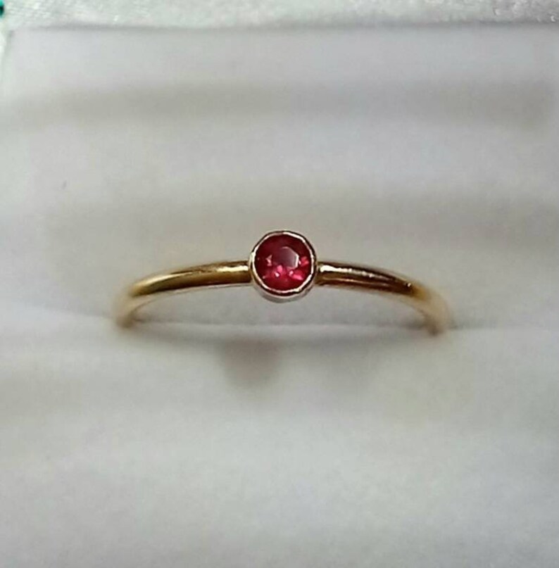 Pu&ograve; includere: Un delicato anello d'oro con una piccola gemma rossa vibrante e rotonda. L'anello ha una fascia sottile e un design semplice ed elegante. La gemma &egrave; incastonata in una lunetta, esaltando il suo colore e la sua brillantezza.