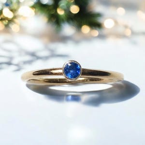 May include: A delicate gold band ring with a single blue sapphire gemstone.