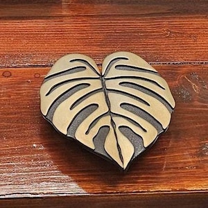 Może przedstawiać: Trzy złote metalowe podkładki w kształcie liścia z ciemnobrązowym obramowaniem. Podkładki są ułożone w rzędzie na drewnianej powierzchni.