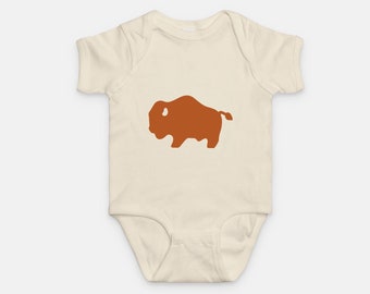 May include: A cream-colored baby onesie with a brown silhouette of a buffalo on the front.