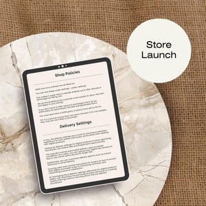 May include: A tablet screen displaying a guide for Etsy shop owners on setting up shop policies and delivery settings. The text on the screen includes the headings "Shop Policies" and "Delivery Settings". The screen is on a light brown surface.