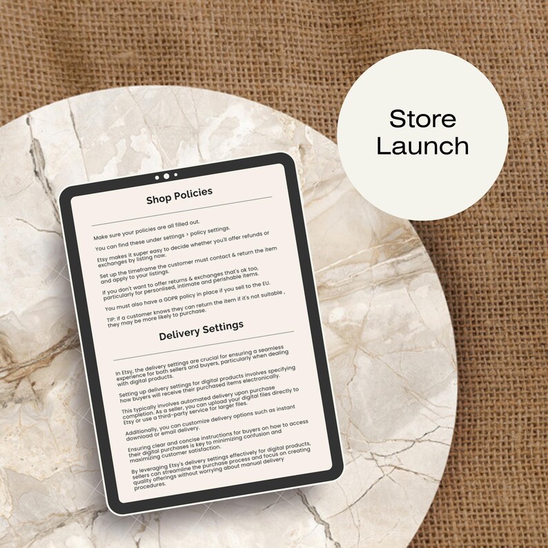 May include: A tablet screen displaying a guide for Etsy shop owners on setting up shop policies and delivery settings. The text on the screen includes the headings "Shop Policies" and "Delivery Settings". The screen is on a light brown surface.