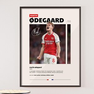 May include: A black and white poster with a photo of a soccer player in a red and white uniform. The player is celebrating a goal with his arms raised. The poster has the text "MARTIN ØDEGAARD '98" at the top and a definition of the word "martin ødegaard" at the bottom.
