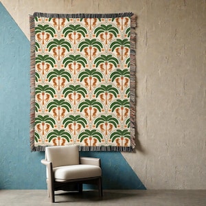 May include: A woven throw blanket with a repeating pattern of green palm trees and orange seahorses on an off-white background. The blanket has a fringed edge and is displayed on a wall with a chair in front.