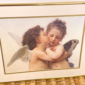 Könnte beinhalten: Gerahmtes Kunstwerk mit zwei cherubinenartigen Figuren, die sich umarmen und küssen. Die Figuren haben lockiges braunes Haar und Flügel. Das Kunstwerk befindet sich in einem goldfarbenen Rahmen mit einem cremefarbenen Passepartout.