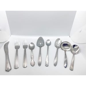 May include: A selection of vintage silverware, including forks, spoons, and serving utensils. The set features various designs, with some pieces showcasing ornate detailing. The silverware is made of a shiny, silver-coloured metal.