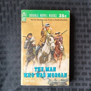 Może przedstawiać: Okładka starej książki w miękkiej oprawie z zielonym i białym tłem. Na okładce przedstawiono scenę z trzema kowbojami na koniach, którzy jadą przez pustynny krajobraz. Tytuł książki to "The Man Who Was Morgan" autorstwa Gene'a Olsona. Książka jest podwójną powieścią i kosztuje 35 centów.