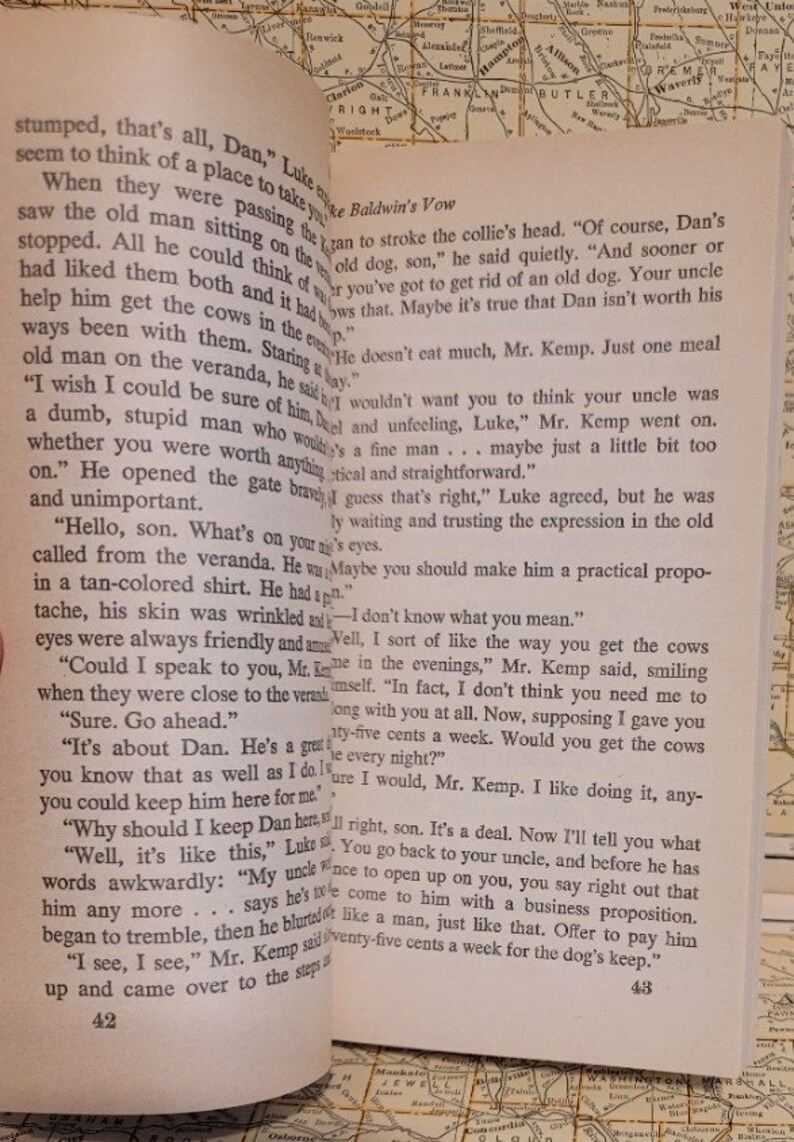 May include: A close-up of an open book with text about a man named Dan and his dog. The text reads, "Of course, Dan's an old dog, son," and "You've got to get rid of an old dog. Your uncle doesn't eat much, Mr. Kemp. Just one meal helps him get the cows in the evenings."