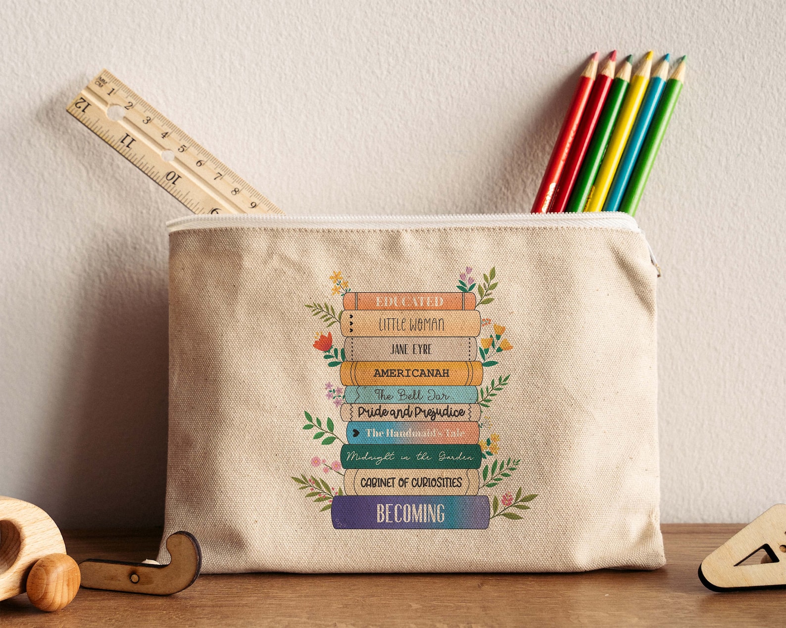 A tan canvas pencil pouch with a couple colored pencils and a ruler sticking out of it. It has 10 book spines on it with different titles, with flowers sticking out of the pages on the sides.