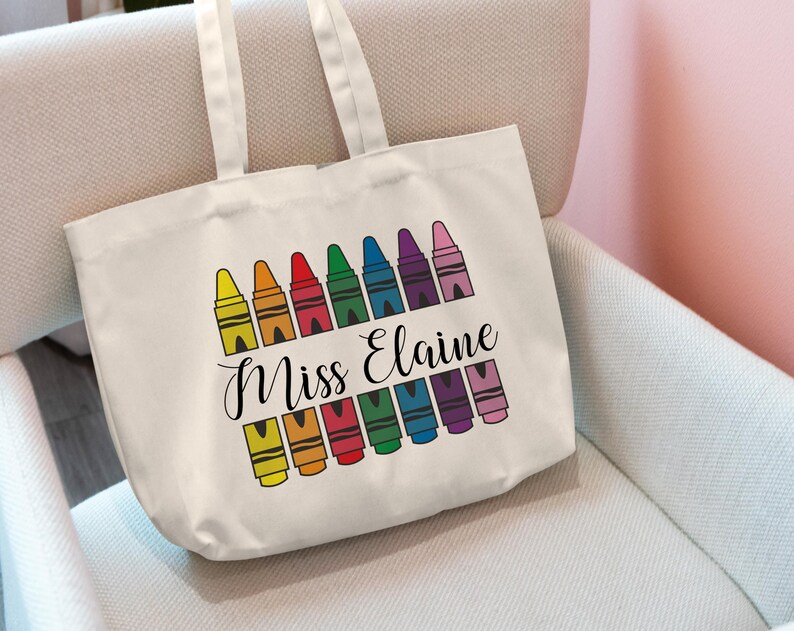 May include: White canvas tote bag with a rainbow of crayons and the text "Miss Elaine" printed on the front.