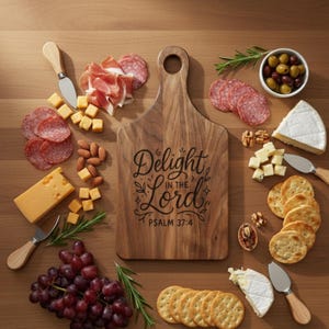May include: A wooden serving board with the text "Delight in the Lord" and Psalm 37:4. The board is surrounded by cheese, crackers, salami, grapes, olives, and nuts. A cheese knife is also present. The board is surrounded by various food items.