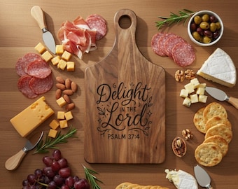 Puede incluir: Una tabla de servir de madera con el texto "Delight in the Lord" y el Salmo 37:4. La tabla está rodeada de queso, galletas, salami, uvas, aceitunas y nueces. También hay un cuchillo para queso.