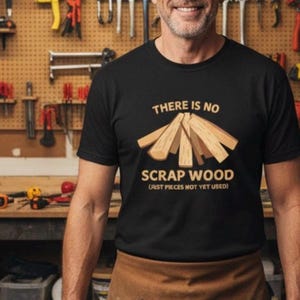 May include: Black t-shirt with the text "THERE IS NO SCRAP WOOD (JUST PIECES NOT YET USED)" and a graphic of wooden planks. The shirt is worn by a person in a workshop setting.