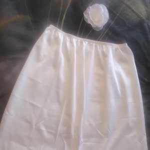 May include: A white satin slip with a lace trim. The slip is a full length and has a smooth, silky texture.