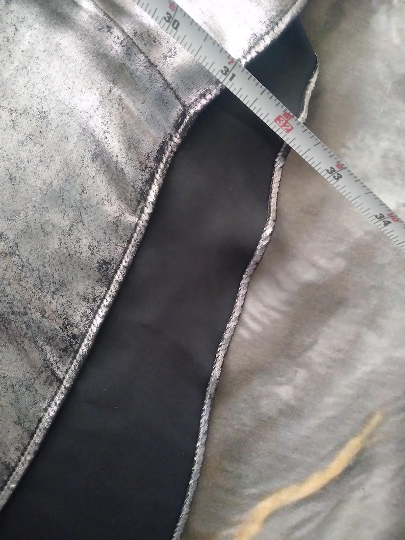 May include: Close-up of a silver fabric with a black fabric seam. A measuring tape is visible with the numbers 30, 31, 32, 33, 34, and 35 inches.