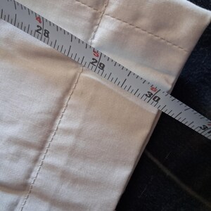May include: Close-up of a light-colored fabric with a measuring tape across it. The tape shows measurements from 28 to 30 inches. The fabric has visible seams and a soft texture, suggesting it might be a piece of clothing or home decor.