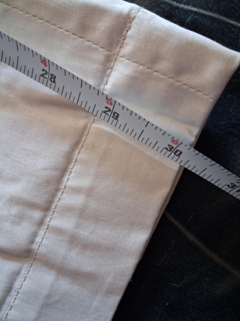 May include: Close-up of a light-colored fabric with a measuring tape across it. The tape shows measurements from 28 to 30 inches. The fabric has visible seams and a soft texture, suggesting it might be a piece of clothing or home decor.