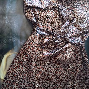 May include: A leopard print robe with a matching tie belt. The robe is a mix of brown, tan, and black, with a silky sheen. The robe is folded, showing the front and the tie belt tied in a bow.