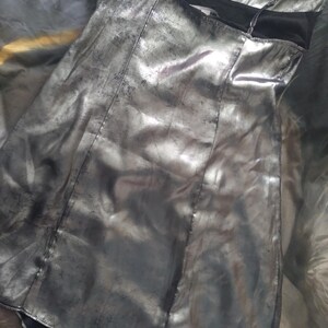 May include: A silver metallic mini dress with a black lining and spaghetti straps. The dress has a slightly A-line shape and a relaxed fit.