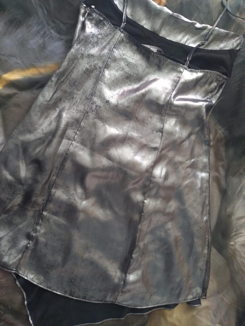 May include: A silver metallic mini dress with a black lining and spaghetti straps. The dress has a slightly A-line shape and a relaxed fit.