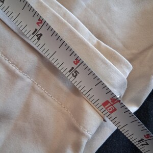 May include: Close-up of tan fabric being measured with a ruler. The ruler shows measurements from 13 to 17 inches. The fabric appears to be part of a garment, possibly pants or a skirt. The fabric is a solid, neutral color.