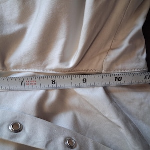 May include: Close-up of a beige garment with a measuring tape laid across it. The tape shows measurements from 6 to 11 inches. The garment has metal eyelets and a seam running across the middle.