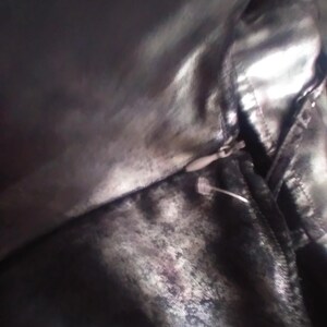 May include: A close-up of a black and silver fabric with a zipper. The fabric has a textured, almost metallic look.